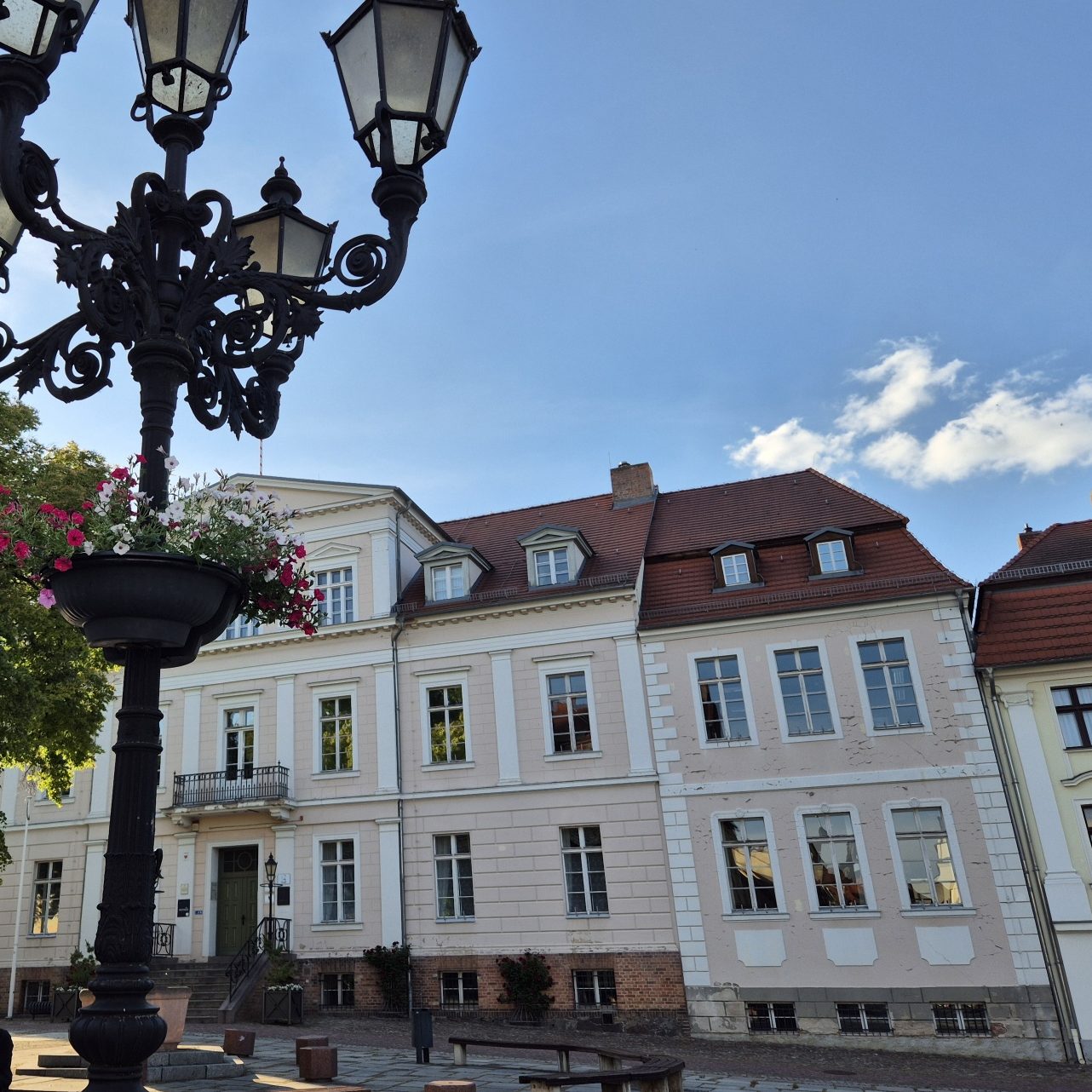 Historisches Gebäude mit Fenstern, umgeben von Bäumen und einem Laternenpfahl.